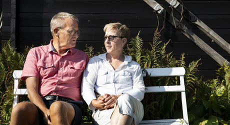 Ægtepar sidder på en bænk i solen og taler sammen