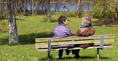 To kvinder sidder på en bænk i en park og taler sammen under corona